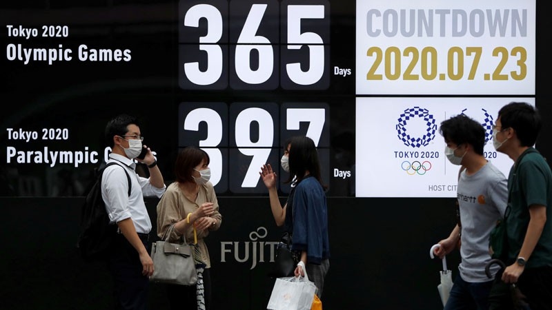 Hành khách đeo khẩu trang đi qua lịch đếm ngược tới kỳ Olympic ở thủ đô Tokyo (Ảnh: Reuters)