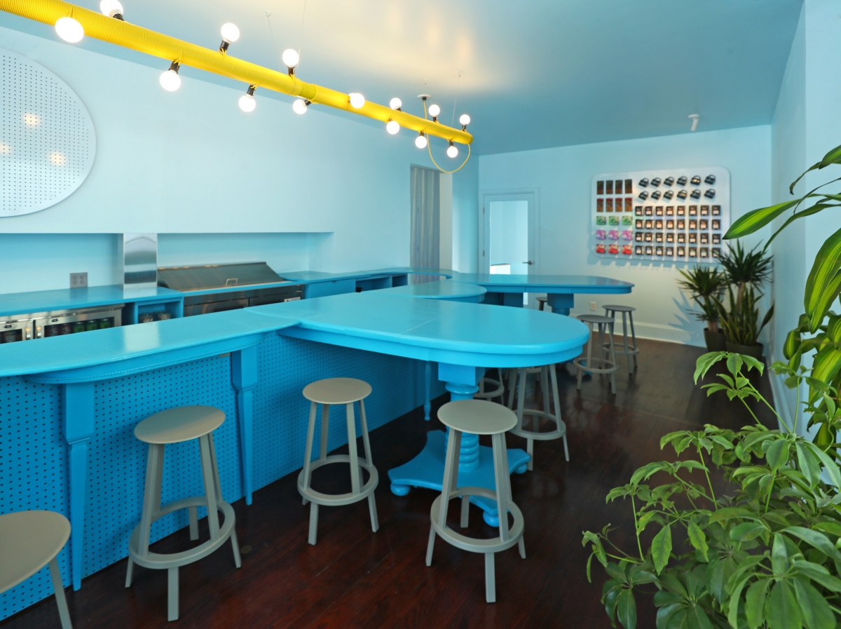 Quầy bar mở có các cụm ghế xoay được bố trí xung quanh các mặt bàn màu xanh lam nhô ra phía khách hàng cho phép dễ dàng giao tiếp giữa khách hàng và nhân viên.