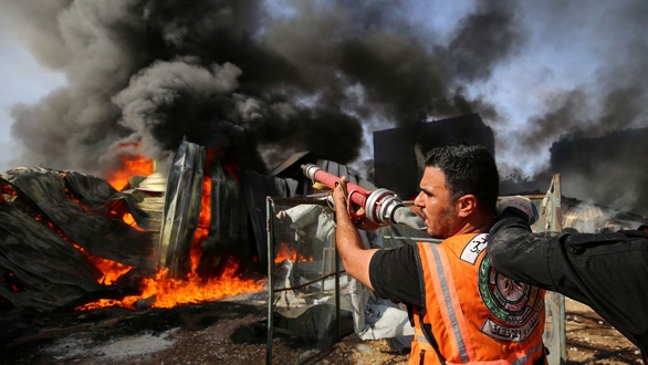 Lính cứu hỏa người Palestine nỗ lực cứu một nhà xưởng trúng đạn của Israel ở phía bắc Dải Gaza ngày 17/5 - Ảnh: REUTERS.