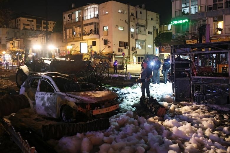 Lực lượng an ninh Israel bên cạnh những chiếc xe trúng rocket của lực lượng Hamas nhằm vào thành phố Holon ngày 11/5. (Ảnh: Reuters)