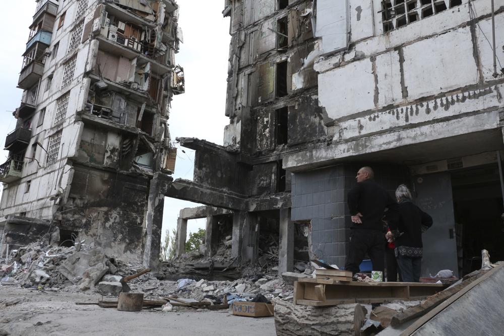 Người dân Ukraine đứng bên ngoài một tòa nhà bị hư hại ở Mariupol. Ảnh: AP